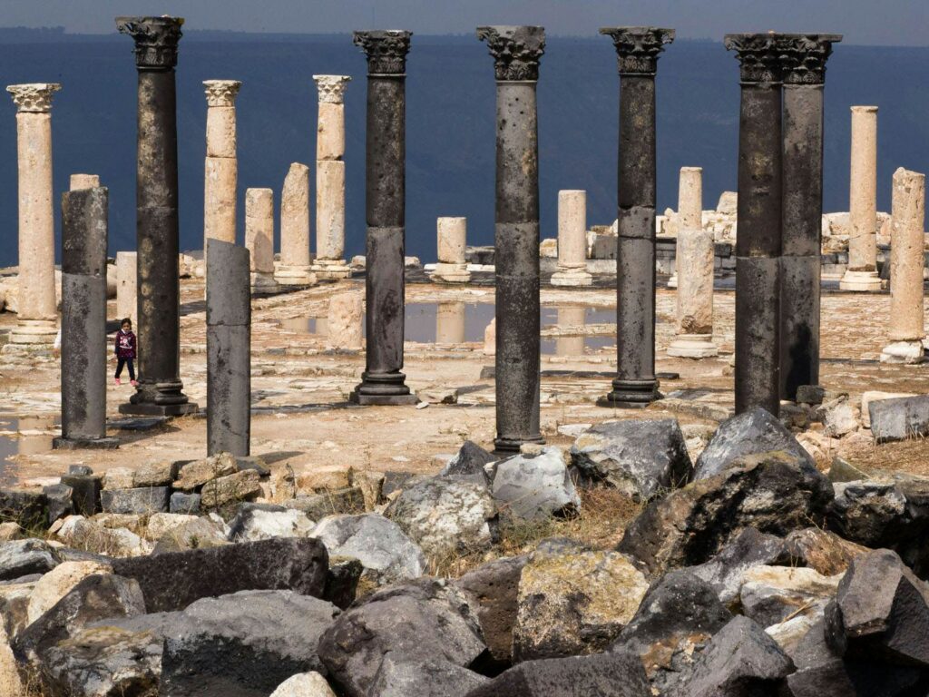 Roman columns and ruins of the ancient city of Gadara (Umm Qais) overlooking a body of water, with a person in the distance.